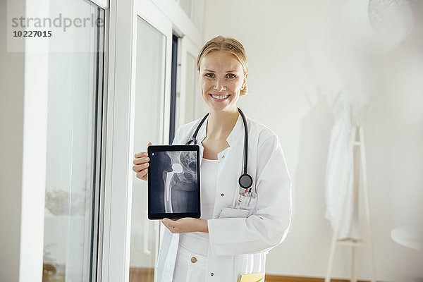 Porträt einer lächelnden Ärztin mit Röntgenbild auf digitalem Tablett