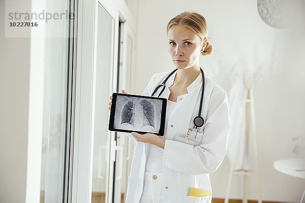 Porträt einer seriösen Ärztin mit Röntgenbild auf digitalem Tablett