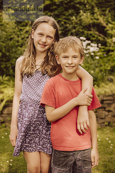 Lächelndes Mädchen legt den Arm um den Bruder im Garten.