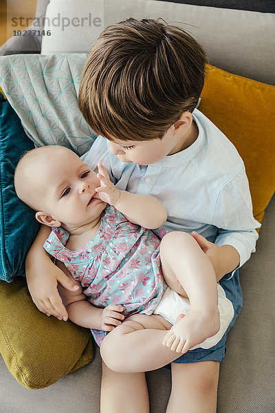 Bruder hält seine kleine Schwester im Arm auf der Couch.