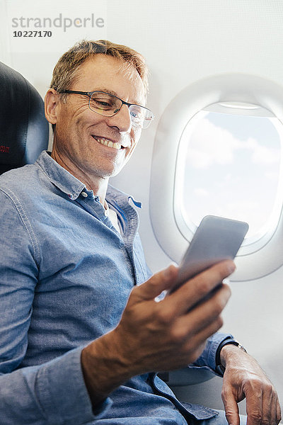 Ein reifer Mann sitzt in einem Flugzeug und schaut auf sein Smartphone.
