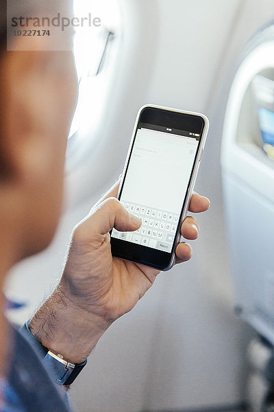 Mann  der in einem Flugzeug sitzt und auf seinem Smartphone tippt.