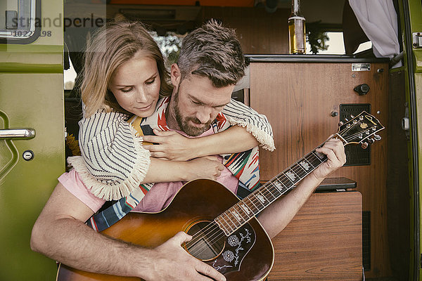 Frau umarmt Mann im Van beim Gitarrespielen