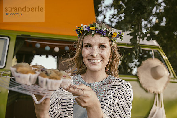 Hippie-Frau präsentiert vegane Muffins vor dem Van