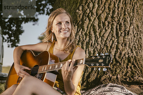 Junge Frau spielt Gitarre am Baum