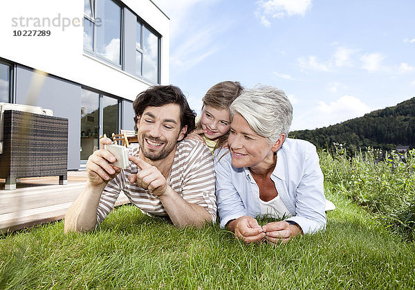 Glückliche Großmutter  Vater und Mädchen auf dem Rasen liegend mit dem Handy