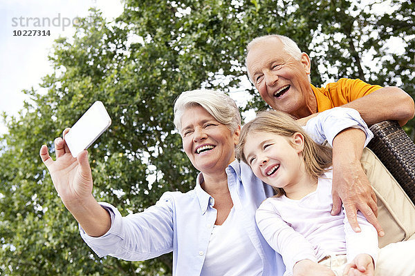 Glückliche Großeltern und Mädchen im Freien  die ein Handyfoto machen.