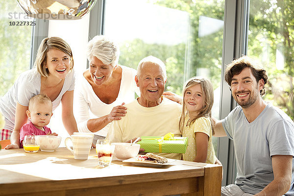 Porträt der glücklichen Großfamilie mit Geschenk am Frühstückstisch