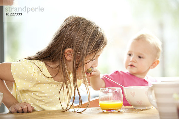 Baby Mädchen füttert Schwester am Frühstückstisch