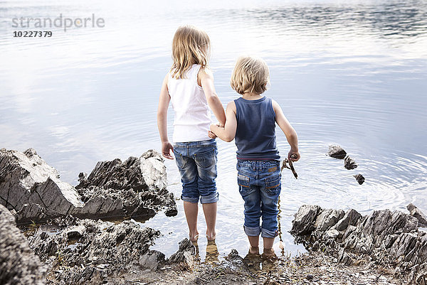 Junge und Mädchen stehen Hand in Hand am Seeufer