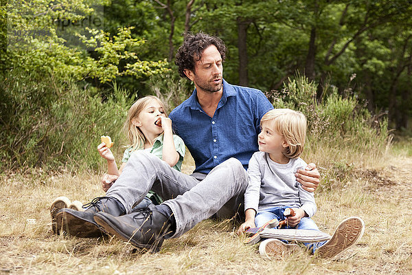 Vater mit zwei Kindern beim Picknick am Waldrand