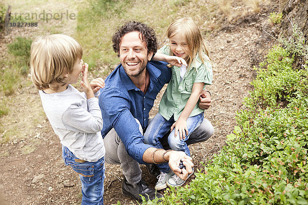 Vater mit zwei Kindern beim Blaubeerensammeln in der Natur