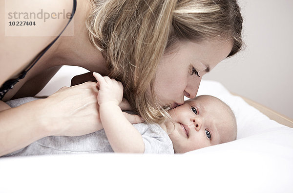 Junge Frau küsst Baby auf Wickeltisch liegend