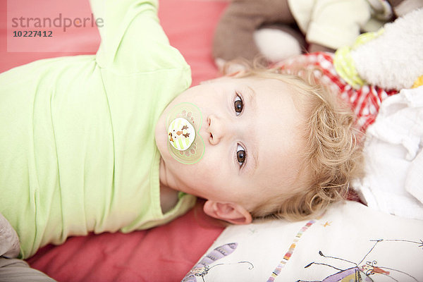 Porträt des kleinen blonden Mädchens mit Schnuller auf dem Kinderbett liegend