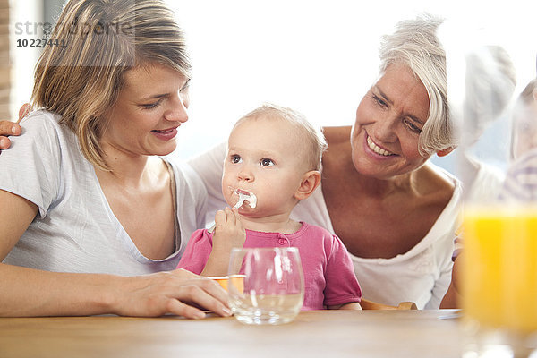 Großmutter und Mutter sehen sich das Mädchen an  das Joghurt isst.