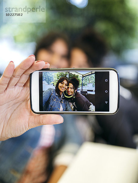 Display des Smartphones mit Fotografie von zwei Frauen  die einen Selfie nehmen.