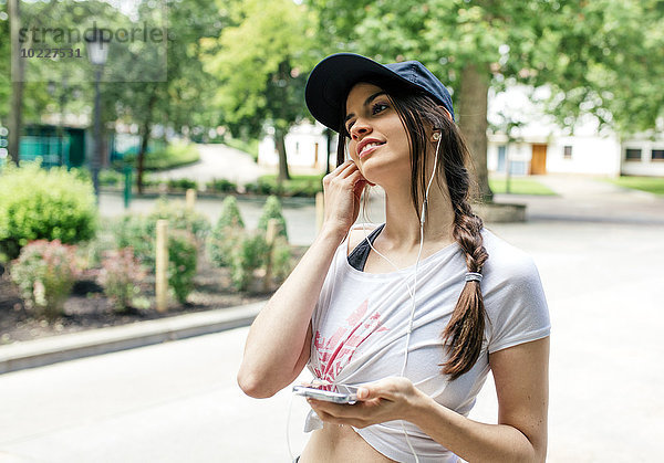 Porträt einer jungen Frau beim Musikhören mit Kopfhörern im Park
