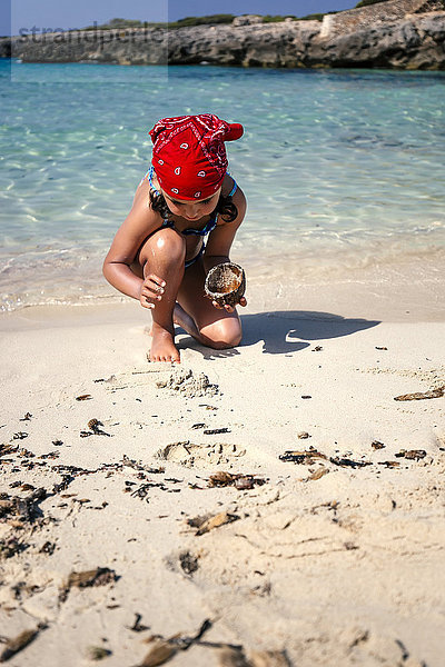 Spanien  Balearen  Menorca  kleines Mädchen spielt am Strand mit einer Kokosnussschale