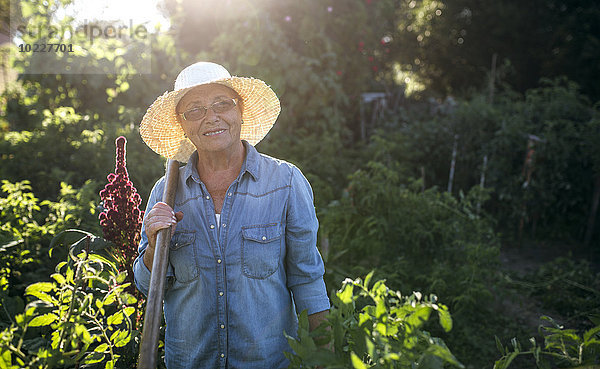 Porträt der lächelnden Seniorin mit Strohhut im Garten