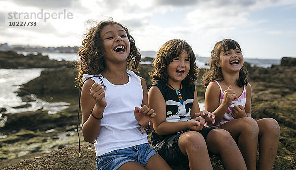 Spanien  Gijon  Gruppenbild von drei lachenden kleinen Kindern an der Felsenküste