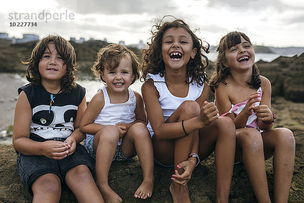 Spanien  Gijon  Gruppenbild von vier kleinen Kindern  die an der Felsenküste sitzen und Spaß haben.