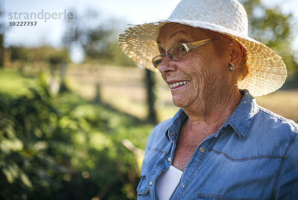 Porträt der lächelnden Seniorin mit Strohhut im Garten