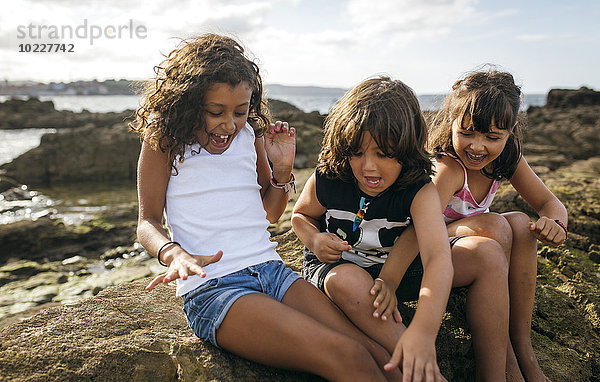 Spanien  Gijon  Gruppenbild von drei aufgeregten kleinen Kindern an der Felsenküste