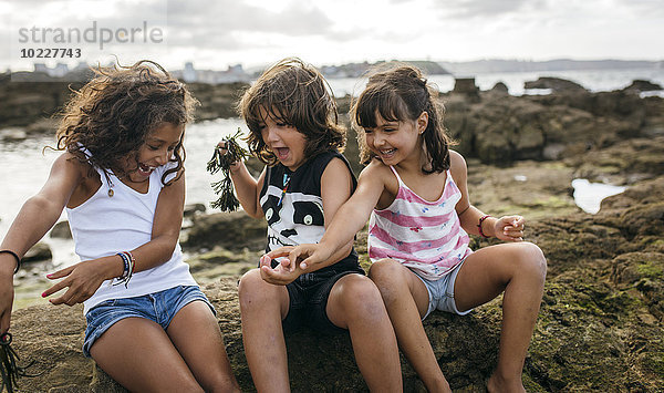 Spanien  Gijon  Gruppenbild von drei aufgeregten kleinen Kindern an der Felsenküste
