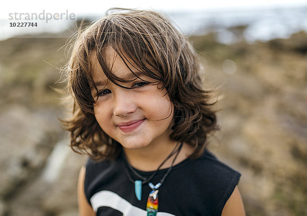 Spanien  Gijon  Porträt eines lächelnden kleinen Jungen mit braunen Haaren an der Felsenküste