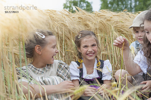 Deutschland  Sachsen  Kinder  die auf einem Getreidefeld sitzen und Spaß haben