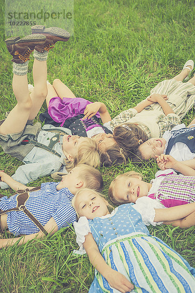 Deutschland  Sachsen  Kindergruppe in traditioneller Kleidung auf einer Wiese im Kreis liegend