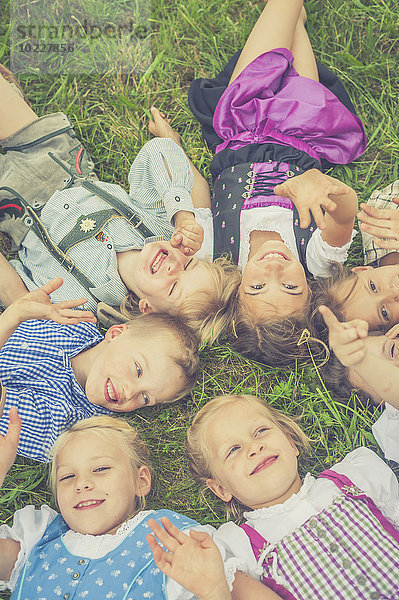 Deutschland  Sachsen  Kindergruppe in traditioneller Kleidung auf einer Wiese im Kreis liegend