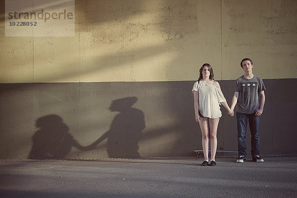 Teenager-Paar steht Hand in Hand vor einer Wand