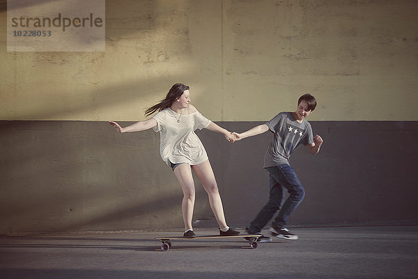 Teenager-Junge zieht seine Freundin auf einem Longboard.