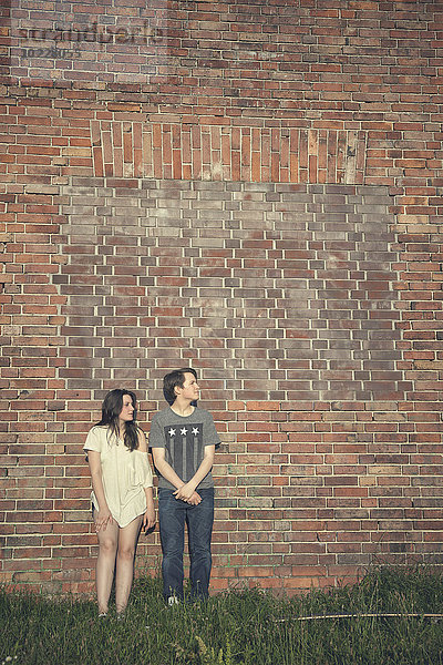 Teenager-Paar vor einer Backsteinmauer stehend