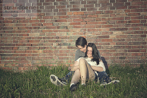 Teenager-Paar auf einer Wiese vor einer Backsteinmauer sitzend