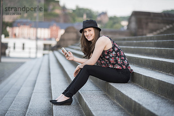 Deutschland  Koblenz  Deutsches Eck  junge Frau mit Handy auf Treppe sitzend
