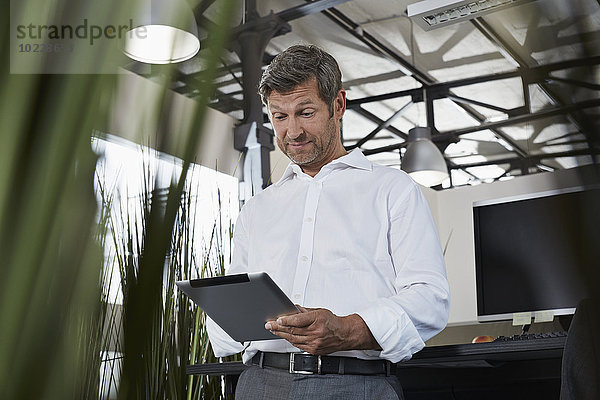 Überraschter Geschäftsmann im Büro mit Blick auf digitales Tablett