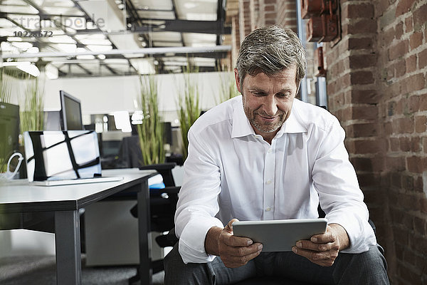 Geschäftsmann im Büro mit Blick auf digitales Tablett