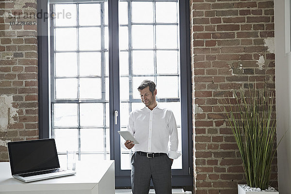 Geschäftsmann am Fenster mit Blick auf das digitale Tablett