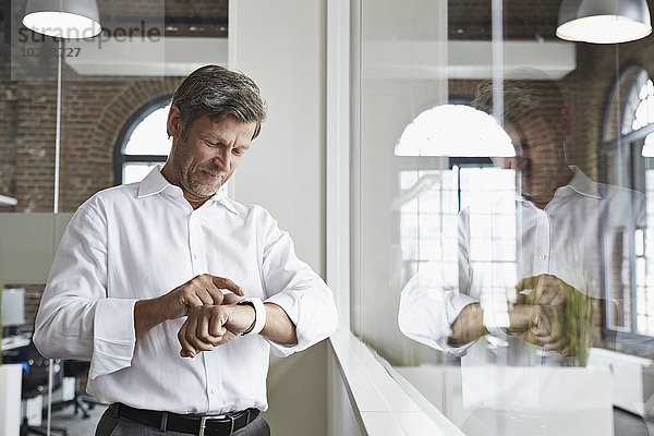 Lächelnder Geschäftsmann im Büro mit Blick auf smartwatch