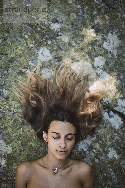 Porträt einer Frau mit geschlossenen Augen  die auf einem Felsen mit zerzaustes Haar liegt.