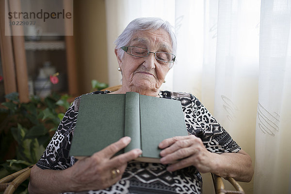 Seniorin bei einem Nickerchen mit Buch in der Hand zu Hause