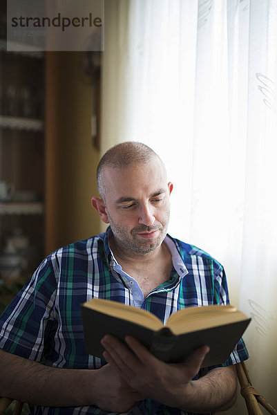 Porträt eines Mannes  der zu Hause ein Buch liest.