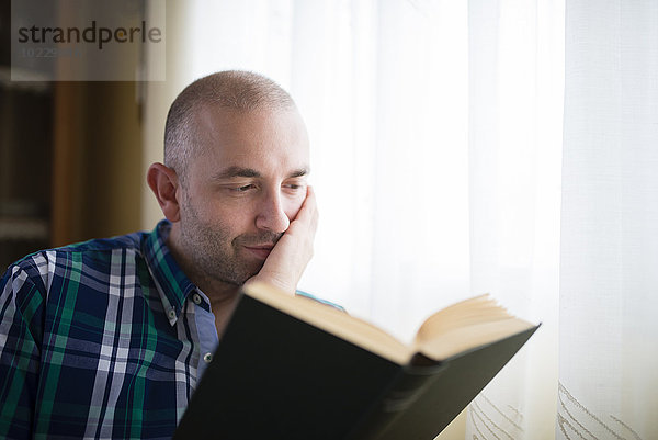 Porträt eines Mannes  der zu Hause ein Buch liest.