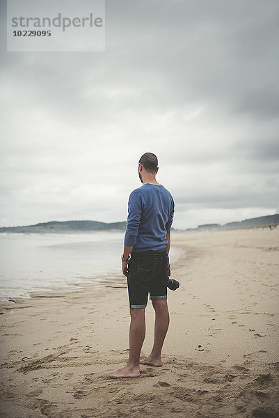 Spanien  Ferrol  Mann mit Kamera am Strand stehend