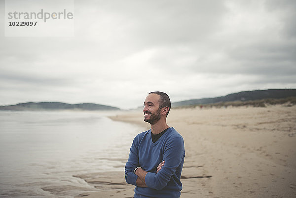 Spanien  Ferrol  Porträt eines lächelnden Mannes mit verschränkten Armen am Strand