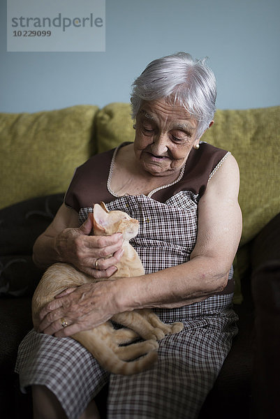 Seniorin streichelt Kätzchen auf dem Schoß liegend