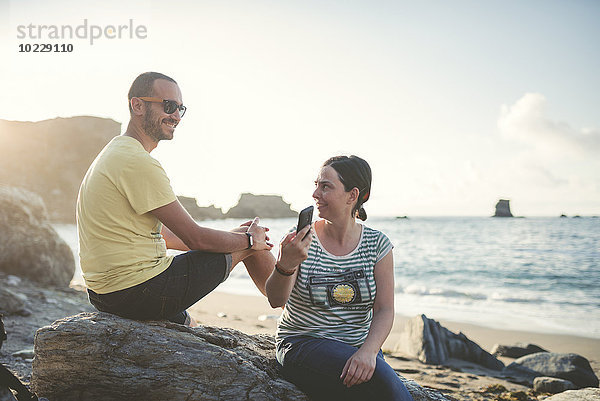 Spanien  Ortigueira  Frau zeigt ihrem Freund Smartphone am Strand