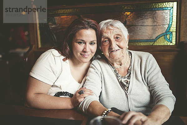 Porträt einer lächelnden Seniorin und ihrer Enkelin  die Kopf an Kopf in einem Restaurant sitzen.